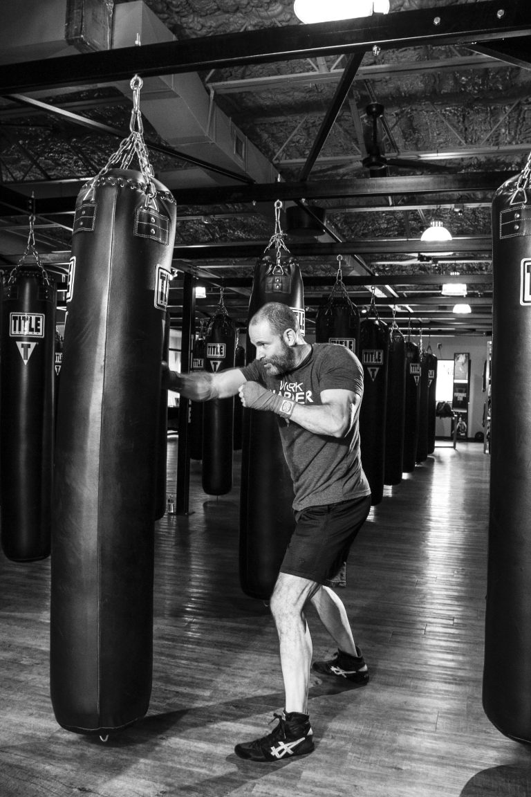 A man boxing with a punching bag in a gym, captured in black and white.