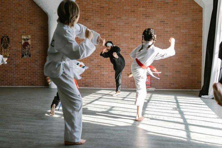 Group of children practicing karate kicks in a dojo with an instructor.