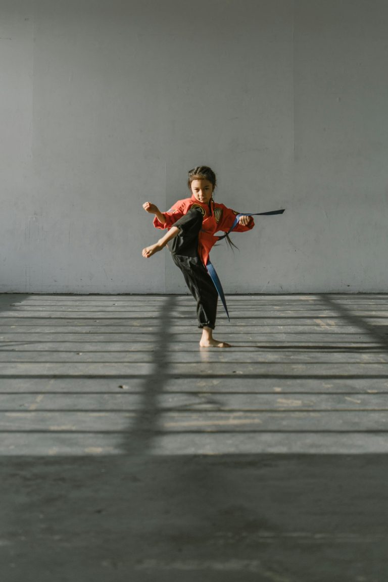 Young girl practicing a high kick in martial arts studio with determination.