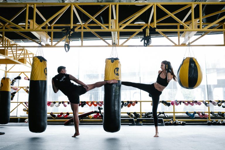 A focused man and woman practice kickboxing in a modern gym setting, showcasing strength and technique.